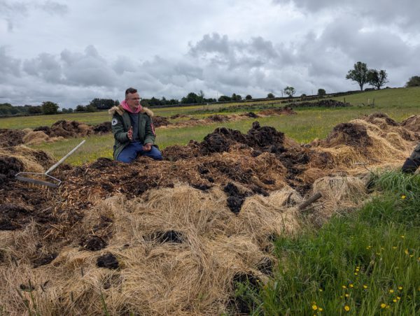 Man talking behind a pile of composting manure and straw