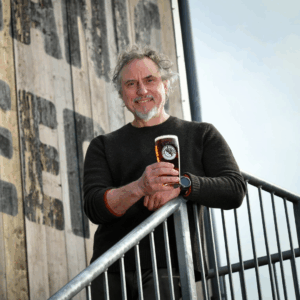 Photo of Greg Pilley leaning on a metal railing holding a beer